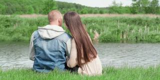 年轻夫妇坐在绿色的草地上。爱情故事，真爱。吻,拥抱。