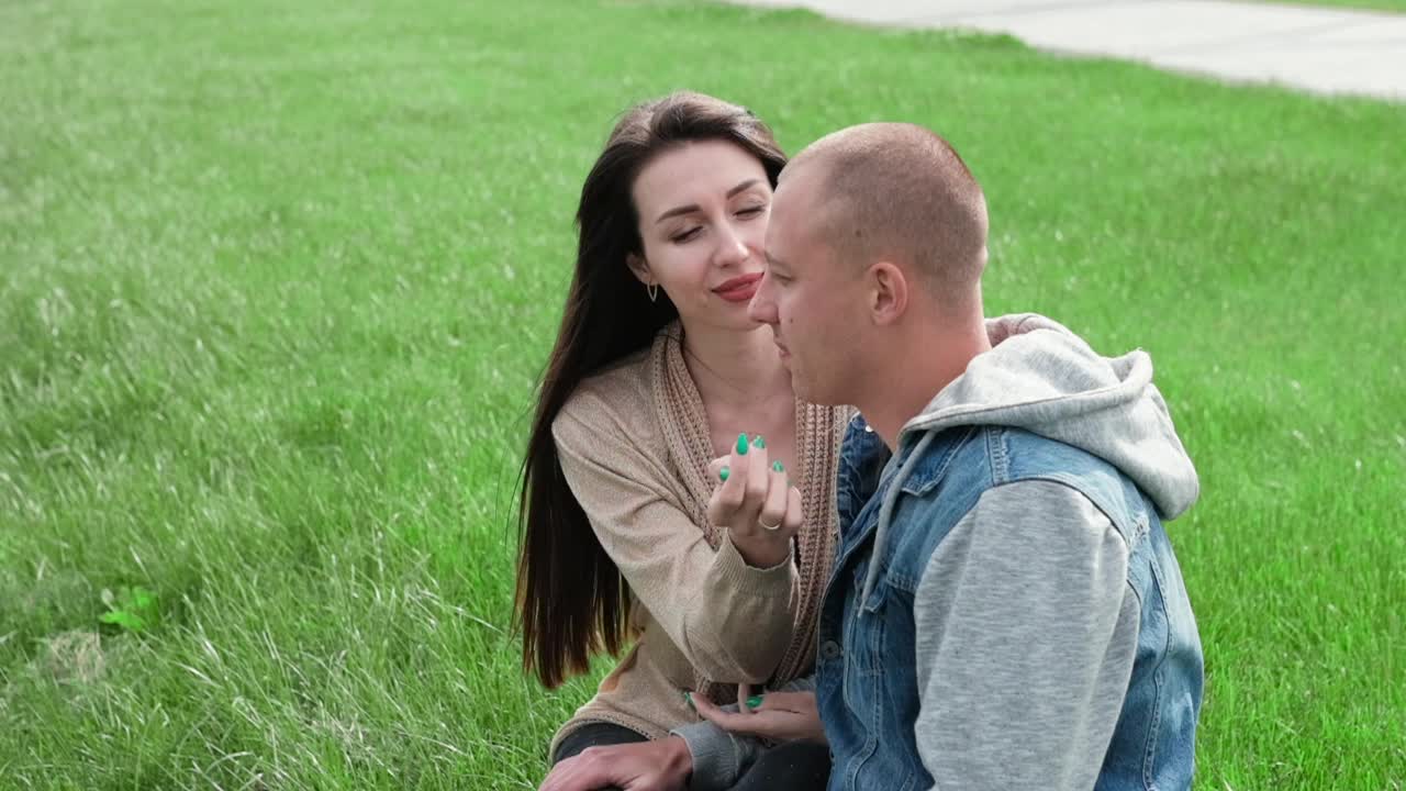 年轻夫妇坐在绿色的草地上。爱情故事，真爱。吻,拥抱。