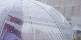 女人站在雨中透明的伞下，在城市恶劣的天气，关闭