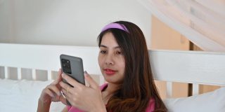 年轻的亚洲女人在酒店的床上使用和触摸智能手机