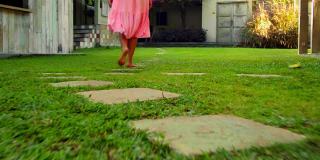 一个欧洲女孩走在有绿色花园和草地的后院，穿着漂亮的粉红色长裙，背过身去