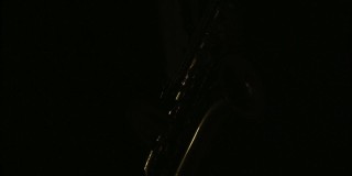 音乐家在黑暗中演奏萨克斯管，在工作室的灯光下照明。演奏萨克斯风的概念