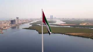 阿联酋国旗和Ras al Khaimah酋长国空中城市景观的标志性天际线上升在阿联酋北部的红树林和小溪视频素材模板下载