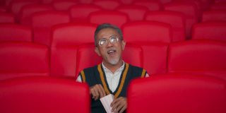 广角正面亚洲华人活跃的老人享受他的零食，同时在电影院看电影，电影院独自