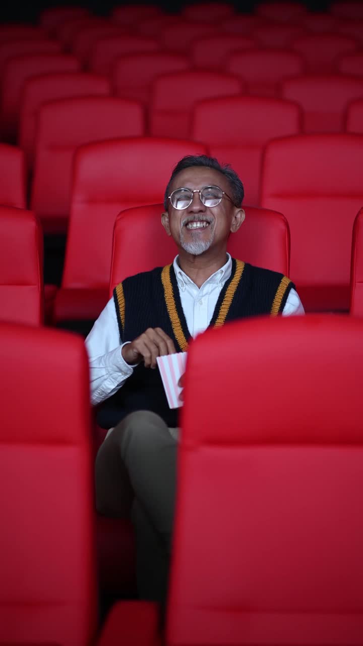 亚洲华人活跃的老人独自在电影院边看电影边吃零食