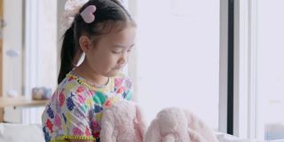 亚洲女孩玩粉红色的兔娃娃。