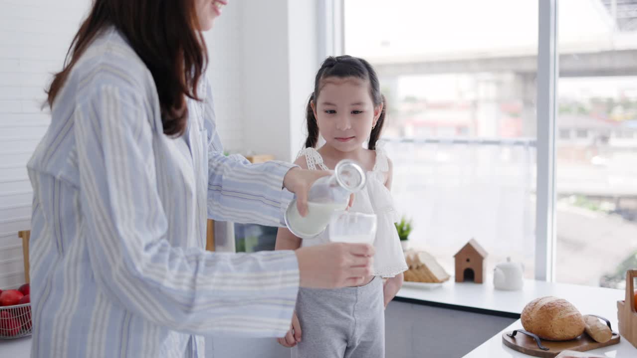 母女俩在家里的厨房里开心地喝着鲜奶。牛奶对孩子的身体发育有好处。家庭与爱生活在一起。周末活动快乐家庭生活理念