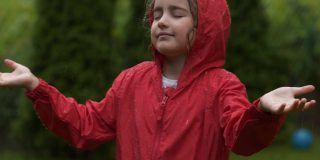 快乐的小女孩在雨中微笑。孩子热爱自然，幸福自由。孩子玩雨滴雨。孩子在下雨的夏天在户外玩耍。穿红雨衣的女孩欣赏秋日降雨。