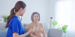 亚洲护士在养老院照顾残疾老年妇女。美丽的治疗师医生在沙发上用听诊器测量女性老年病人的心率。医疗保险服务理念。