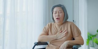 亚洲老年残疾妇女在轮椅上心脏病发作。老年女性胸痛，呼吸困难，紧抓胸部剧烈疼痛。医院保健和医疗理念。