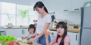 亚洲幸福的家庭，母亲花时间与年幼的女儿在厨房。可爱美丽的父母妈妈和小妹妹可爱的女孩孩子感到高兴，在家享受吃苹果健康。健康食品的概念