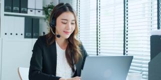 亚洲美丽的商业女性在办公室微笑的肖像。漂亮的职业装女职员坐在工作场所的桌子上，用笔记本电脑看镜头。