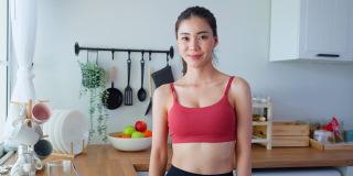 亚洲活跃女人的肖像在运动服看相机在屋里。美丽的运动女孩喜欢吃干净的沙拉，在家里和交叉双臂的健康运动后。饮食和健康食品的概念。