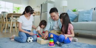 亚洲幸福的一家人坐在地板上，在客厅里一起玩儿童玩具。漂亮的父母，母亲和父亲花时间与年幼的女儿在家里。家庭活动关系概念。