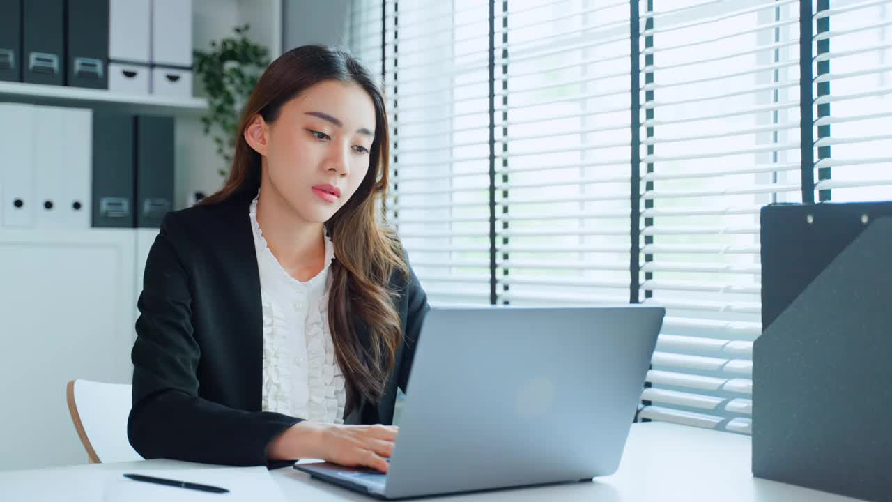 疲惫迷人的亚洲女商人在工作桌上看着许多文件工作。忙碌的女员工由于工作到很晚，在办公室的电脑桌上放着工作文件，感到疲惫头痛