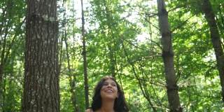 一个快乐的年轻女孩穿着白色飘逸的裙子跑上树林中的堤坝