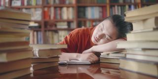 疲倦的亚洲学生睡在一堆书，休息学习