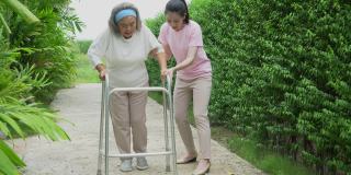 亚洲的高级马瑟与沃克和成年的女儿在花园里散步。老妇残疾人步行和照顾年轻妇女帮助后院公园户外。保健家庭生活方式