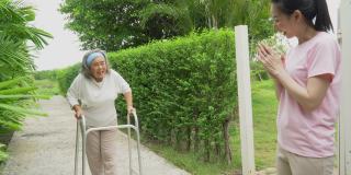 亚洲的高级马瑟与沃克和成年的女儿在花园里散步。老妇残疾人步行和照顾年轻妇女帮助后院公园户外。保健家庭生活方式