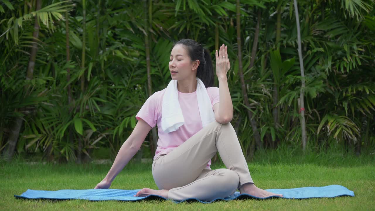 年轻的亚洲健身女子练习瑜伽伸展她的腿，以暖身坐在垫在公园早上。运动适合女孩锻炼或锻炼训练后院在家里的生活方式的概念