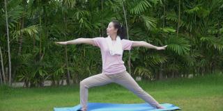 年轻的亚洲健身女子练习瑜伽伸展她的腿，以暖身坐在垫在公园早上。运动适合女孩锻炼或锻炼训练后院在家里的生活方式的概念