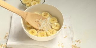 一个男人用木勺把燕麦粥和香蕉片混合在一起。