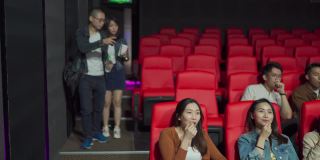 在电影放映时间，一对亚洲中国夫妇进入电影院，试图穿过其他观众到达他们的座位