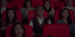 坏习惯粗鲁的亚洲中国老人在电影放映期间大声讲电话，在黑暗中打扰和忽视他周围的其他观众。一个女孩把手指放在嘴唇上，轻拍他的肩膀，让他保持安静