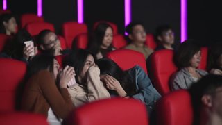 亚洲的中国女人在电影院看恐怖的惊悚电影，和其他观众一起看视频素材模板下载