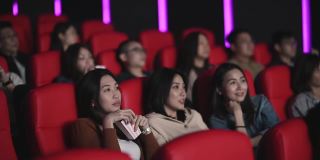 亚洲的中国女人在电影院看恐怖的惊悚电影，和其他观众一起看