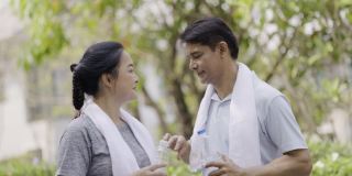 一对亚洲老夫妇在乡村花园锻炼，脸上挂着幸福的微笑。锻炼使你健康。喝塑料瓶里的水可以清除汗水。周末活动快乐家庭生活理念。