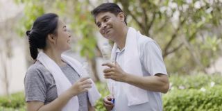 一对亚洲老夫妇在乡村花园锻炼，脸上挂着幸福的微笑。锻炼使你健康。喝塑料瓶里的水可以清除汗水。周末活动快乐家庭生活理念。