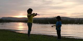 亚洲两个孩子在日落时在湖边玩泡泡的场景，快乐的时光，为孩子们的节日活动