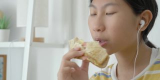 亚洲女孩一边吃着火腿烤面包一边用智能手机看电影，生活理念。