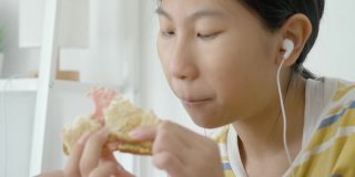 亚洲女孩一边吃着火腿烤面包一边用智能手机看电影，生活理念。