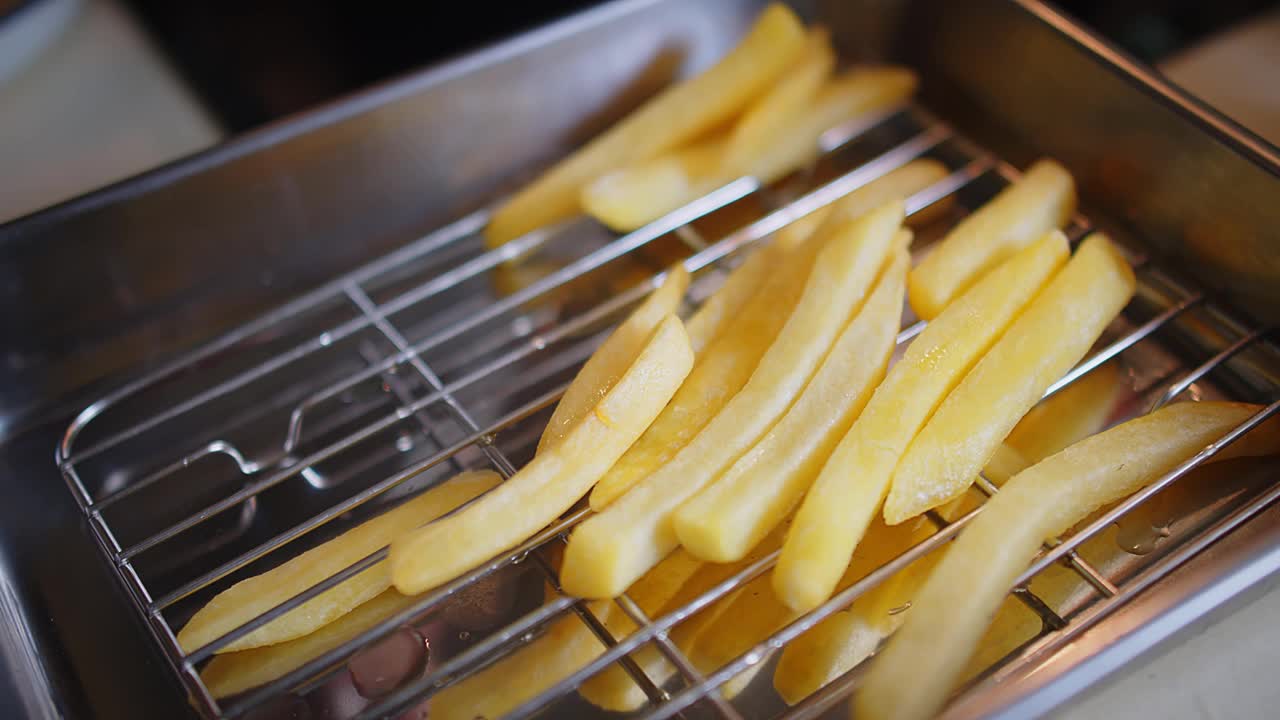 在厨房里用钳子夹着热炸的黄色薯条，油炸美味的小吃，快餐店