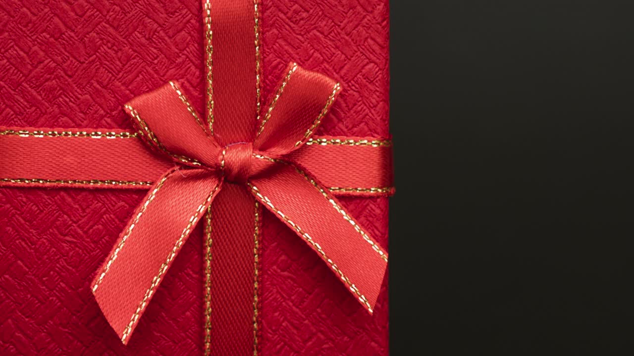 漂亮的红色礼品盒，黑色背景上有一个小蝴蝶结。一个伟大的礼物