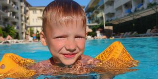 孩子们正在学习游泳，水上安全，小男孩穿着黄色充气套衫在室外游泳池游泳