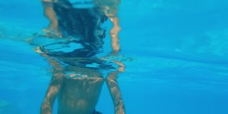 孩子睁着眼睛潜到水下，小男孩在暑假期间在游泳池的蓝色水里游泳