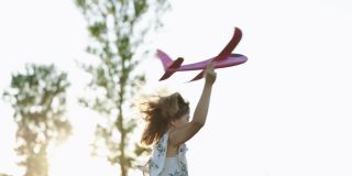女孩带着玩具飞机在夕阳下的田野上奔跑。孩子们玩玩具飞机。青少年梦想飞行，成为一名飞行员。女孩想成为一名飞行员和宇航员