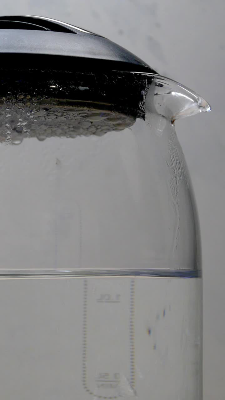 在浅色背景下，透明的玻璃电水壶里沸腾着带有气泡的沸水。