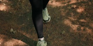 徒步旅行的概念。脚穿着运动鞋在地上走。前视图。一个女人在夏天的森林里徒步旅行。实时