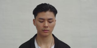 年轻的亚裔男学生的肖像，站在室外的白墙上向上看