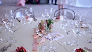 精美的圆桌安排在婚礼上，水晶葡萄酒和香槟酒杯和银餐具在象牙桌布上。餐桌中央摆着一束杏花。时尚的节日婚礼装饰，精美视频素材模板下载