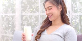 健康亚洲年轻女性在家里喝含钙牛奶强健骨骼，微笑印度女性拿着玻璃豆奶享受营养健康生活，健康与天然牛奶新鲜概念