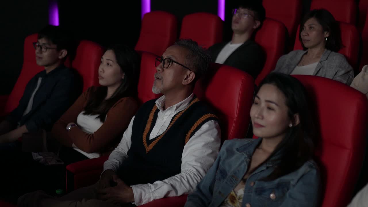 一位亚裔中国老人在电影院看电影时使用智能手机。打扰她周围的观众