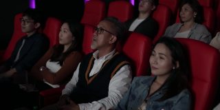 一位亚裔中国老人在电影院看电影时使用智能手机。打扰她周围的观众