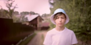 一个严肃悲伤的男孩的肖像戴着帽子看着摄像机在村庄，斯坦尼康电影拍摄
