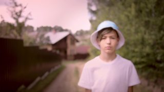 一个严肃悲伤的男孩的肖像戴着帽子看着摄像机在村庄，斯坦尼康电影拍摄视频素材模板下载