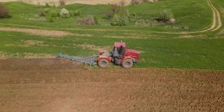 红色拖拉机正用耙子松动地面，防止土壤干燥，平整地面，消灭杂草，准备季节性种植小麦，无人机从高度、侧面拍摄
